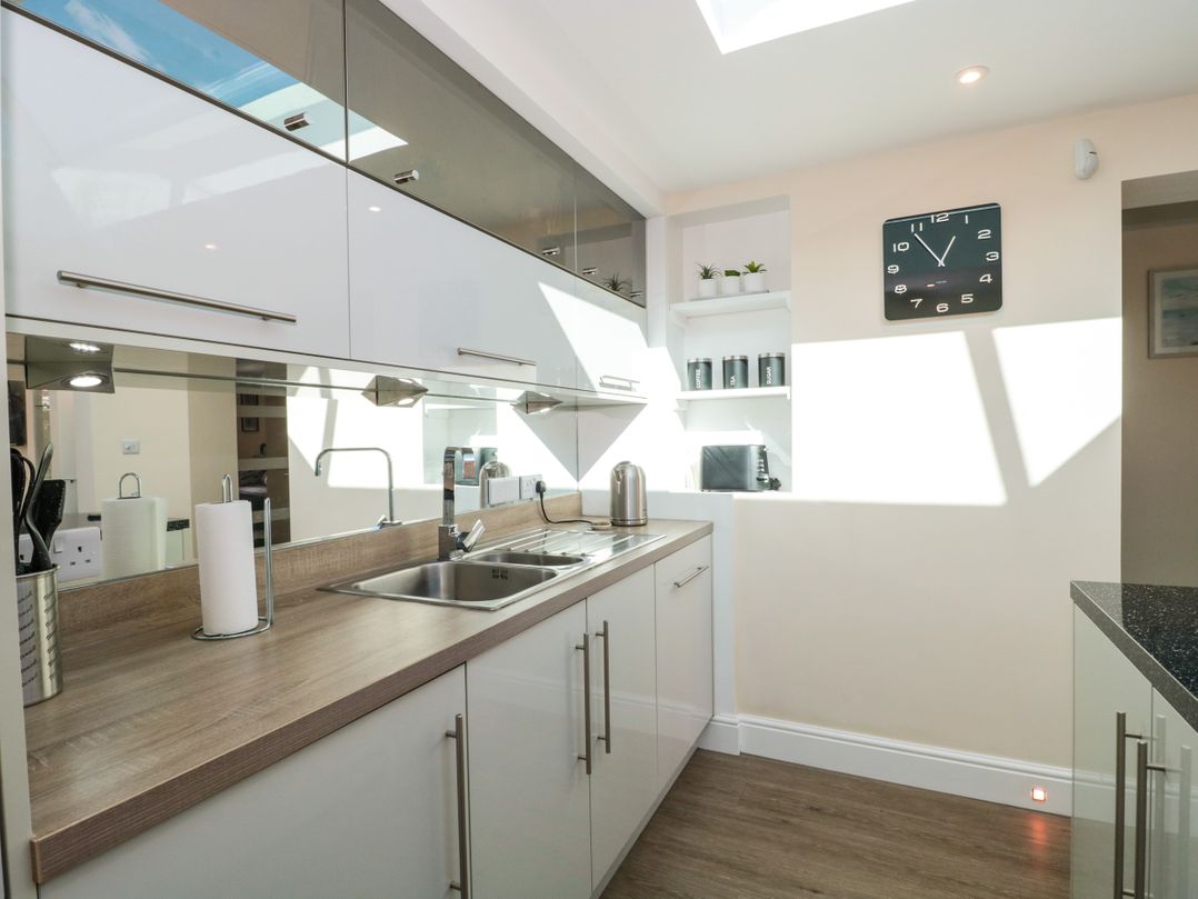 A kitchen with a wooden countertop a sink a kettle a paper towel holder wall cabinets and a clock at Minime in Weston-Super-Mare