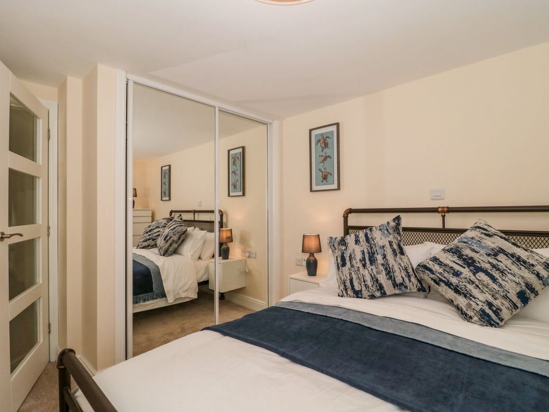 A bedroom with a bed pillows bedside table lamp mirrored wardrobe and wall art at Minime in Weston-Super-Mare