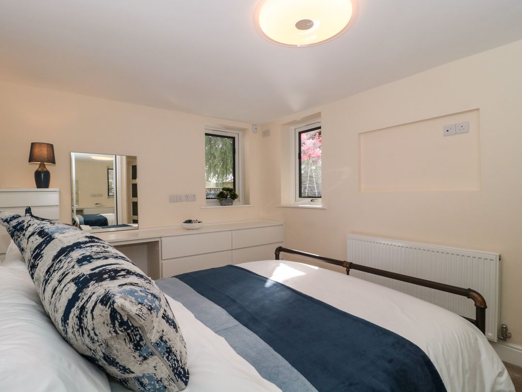 A bedroom with a bed and a large pillow a dresser with a mirror and a lamp and two windows at Minime in Weston-Super-Mare