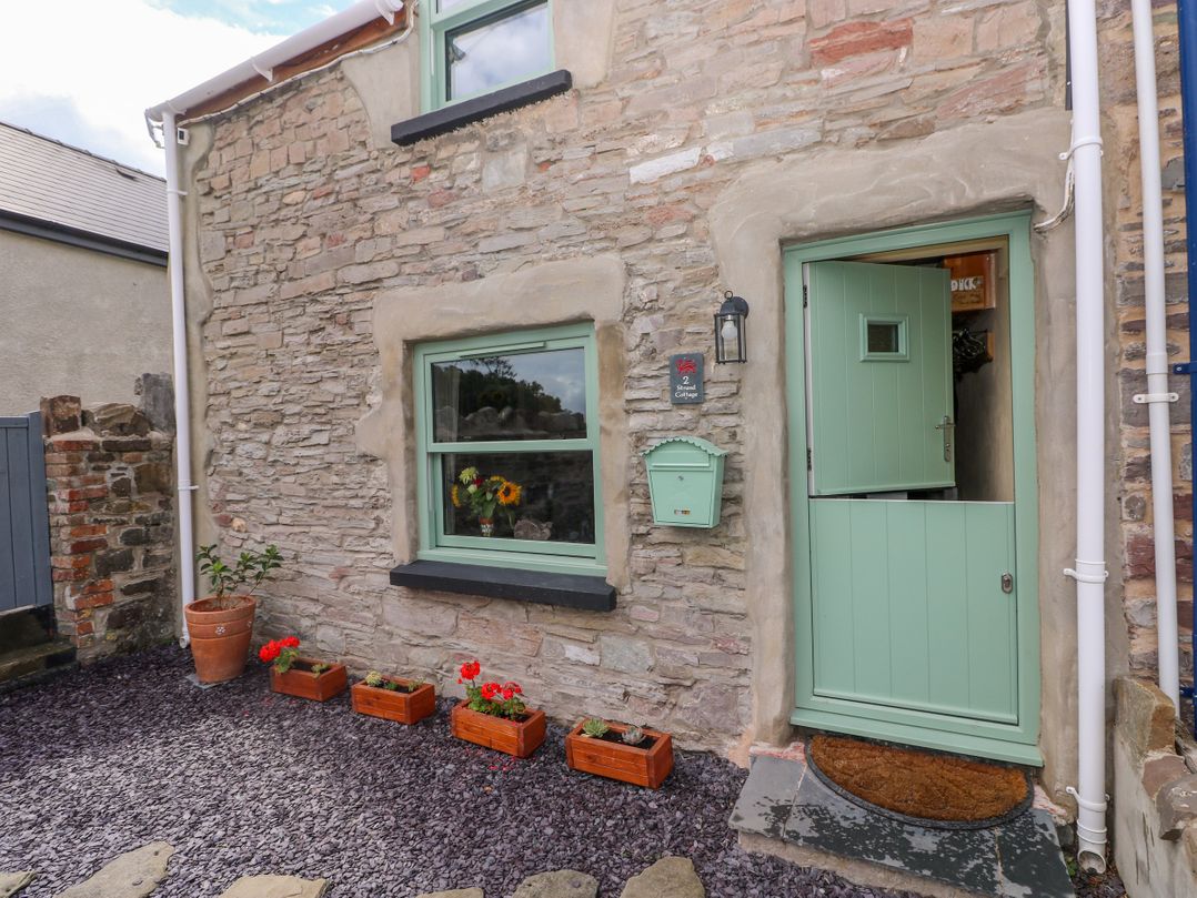 An entrance with a green door and flower pots at 2 Strand Cottages in Laugharne