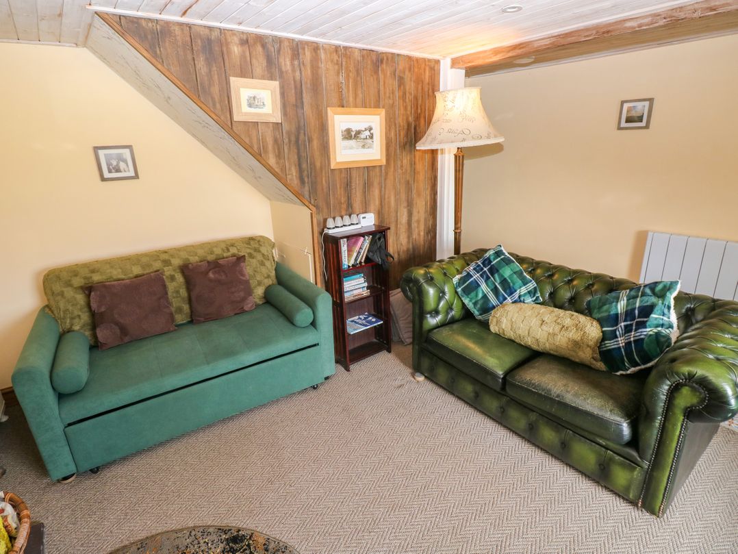 A living room with green and brown sofas and a bookshelf at 2 Strand Cottages in Laugharne