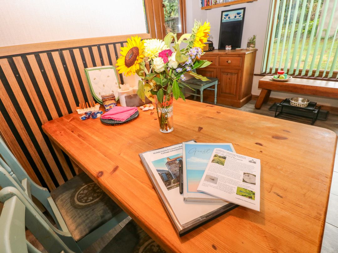 A dining room with a wooden table and flowers at 2 Strand Cottages in Laugharne
