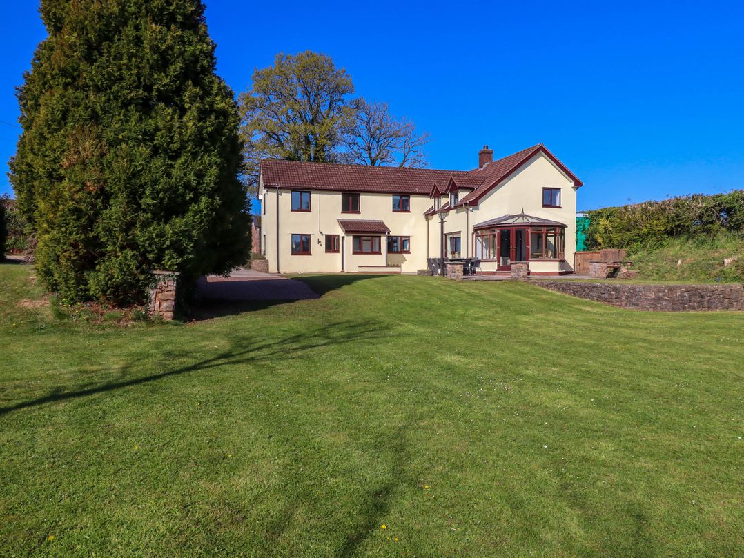 A two-story house with beige walls and brown roof with a large green lawn in front at Valley House in Halberton near Tiverton