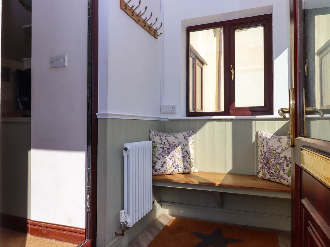 A small entryway with a wooden bench with floral cushions a radiator and a window at Valley House in Halberton near Tiverton