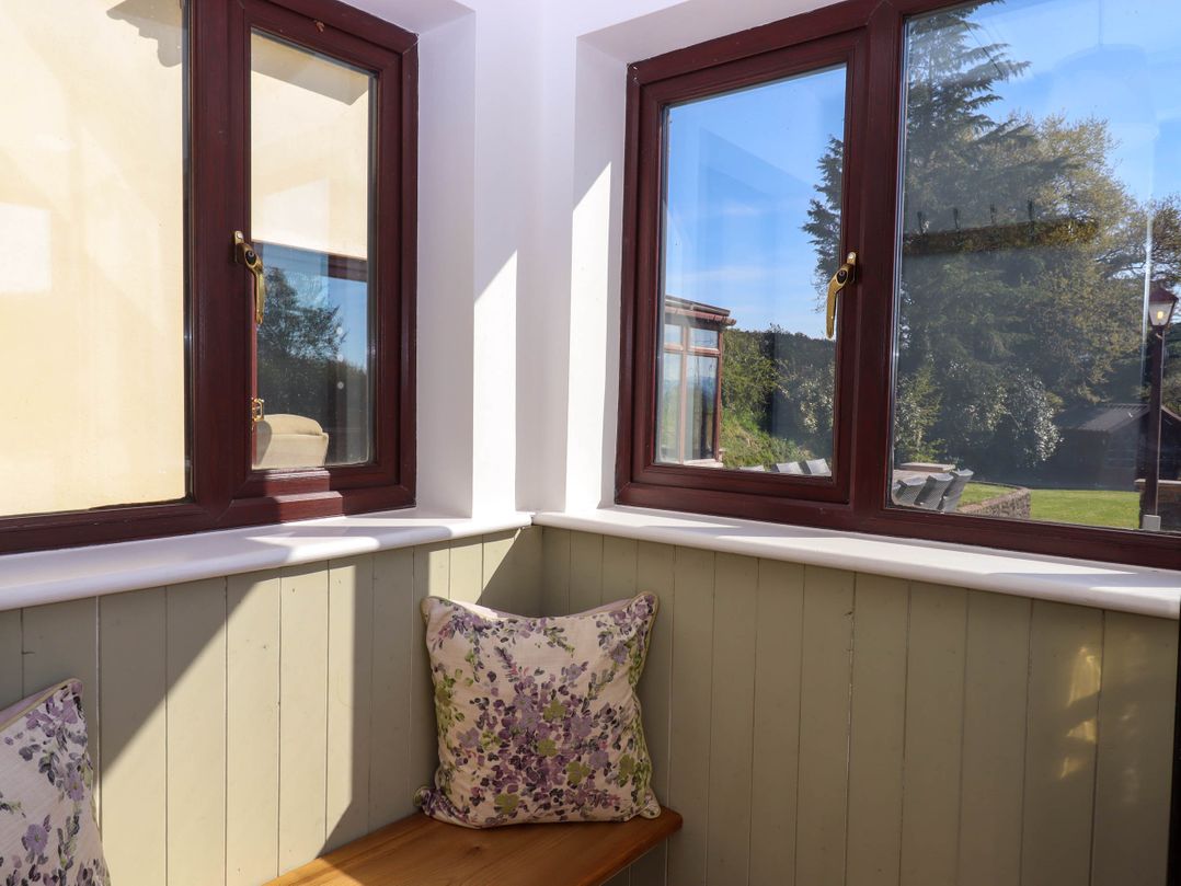 A corner window seat with floral cushions and brown window frames overlooking a garden at Valley House Halberton near Tiverton