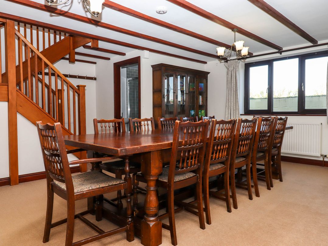 A dining room with a long wooden table and multiple chairs near a staircase and a glass cabinet at Valley House in Halberton near Tiverton
