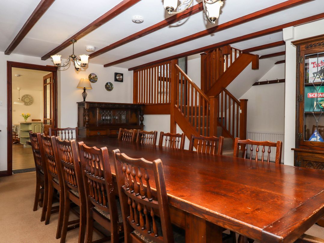 A dining room with a long wooden table and chairs wooden staircase and cabinet at Valley House in Halberton near Tiverton