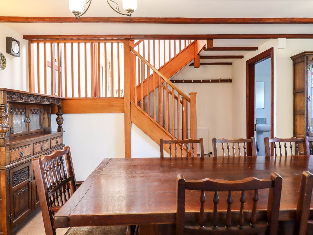 A dining room with wooden table and chairs near wooden staircase and cabinets at Valley House Halberton near Tiverton