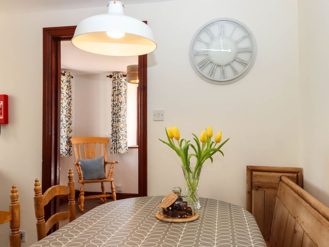 A dining area with a table covered by a patterned tablecloth with yellow tulips in a vase and a plate of brownies under a glass cover at Valley House in Halberton near Tiverton