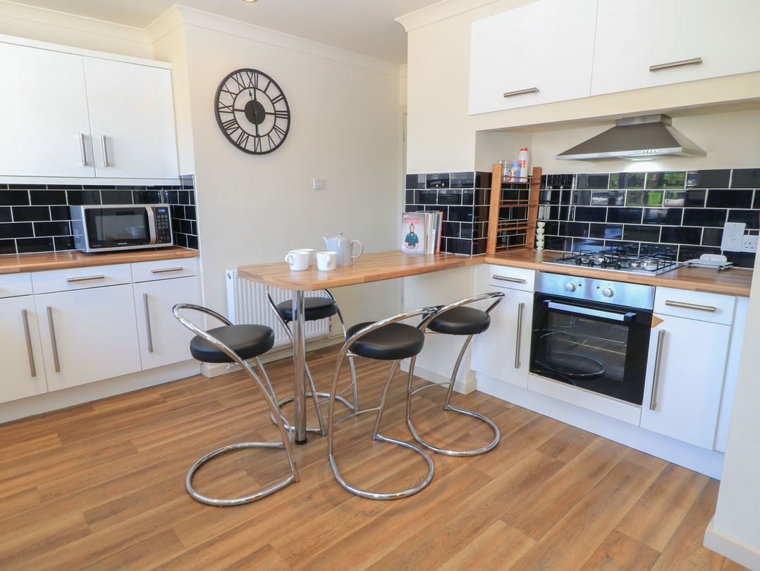 A kitchen with microwave, oven and bar stools at Bayview Cottage in Southbourne