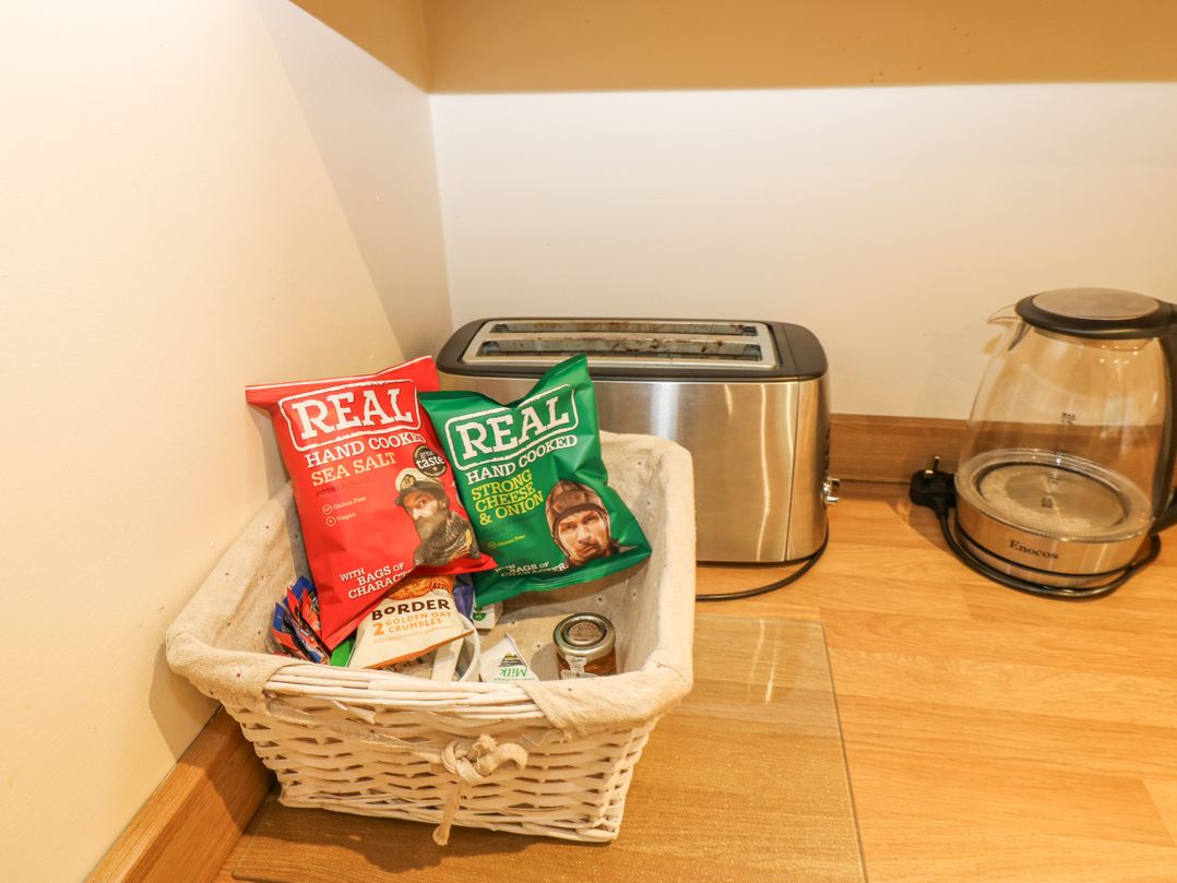 A kitchen countertop with a basket of snacks beside a toaster and a glass electric kettle at Walworth Castle Holiday Cottage Walworth near Darlington