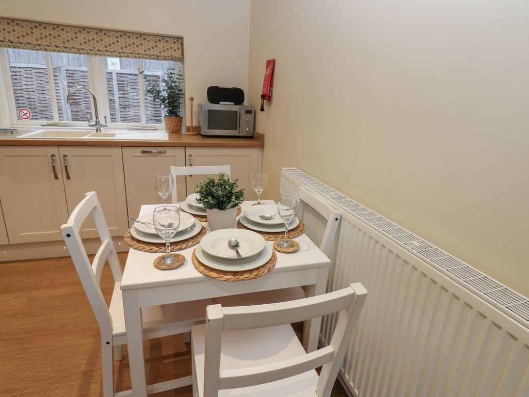 A small kitchen dining area with a white table set for four and kitchen cabinets with a sink at Walworth Castle Holiday Cottage Walworth near Darlington