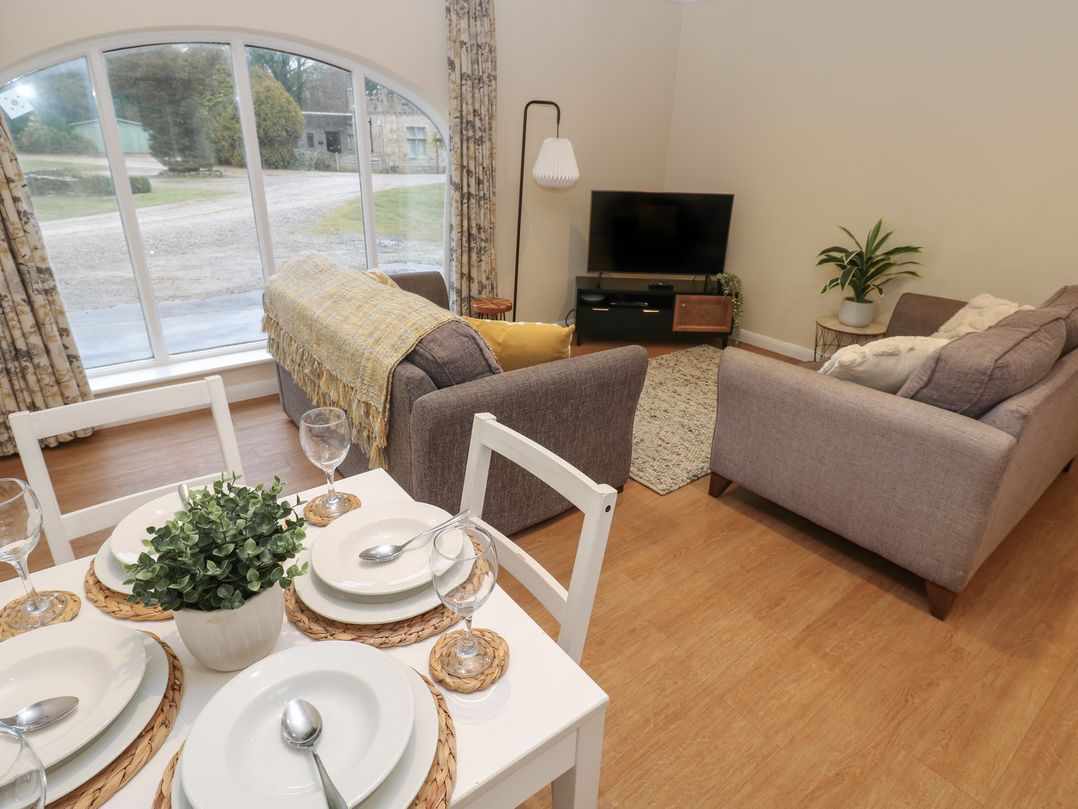 A living room with sofas a television a floor lamp a dining table set with plates and glasses and large windows at Walworth Castle Holiday Cottage Walworth near Darlington