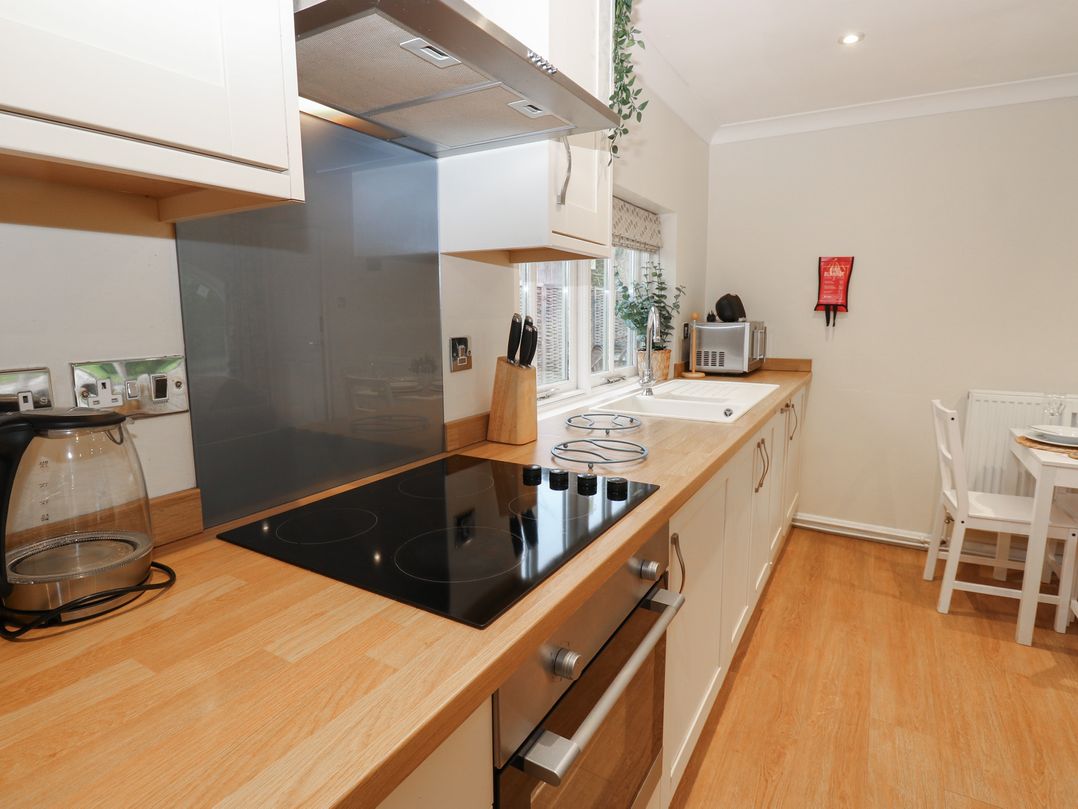 A kitchen with a stovetop oven kettle knives microwave sink and a dining table with chairs at Walworth Castle Holiday Cottage in Walworth near Darlington
