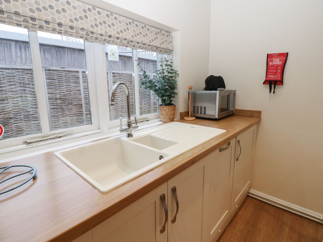 A kitchen countertop with a double sink a plant a microwave and a fire blanket on the wall at Walworth Castle Holiday Cottage in Walworth near Darlington