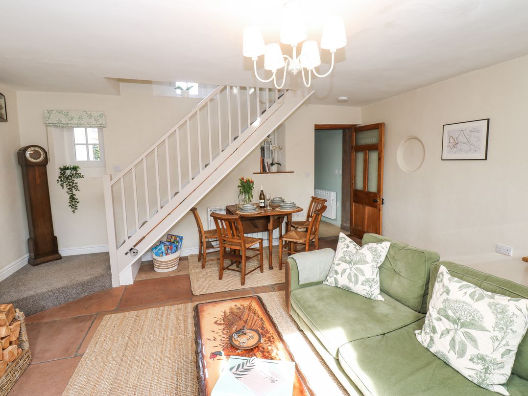 A living room with a green sofa and wooden dining table under white stairs at 3 Eden View in Lazonby