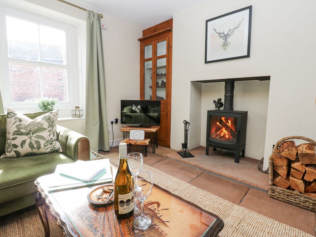 A living room with a green sofa a wood burning stove fire and a bottle of wine on a table at 3 Eden View in Lazonby