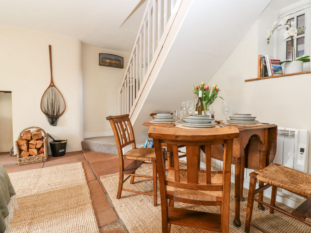 A dining area with wooden table and chairs under a staircase with stacked firewood and a net on the wall at 3 Eden View in Lazonby