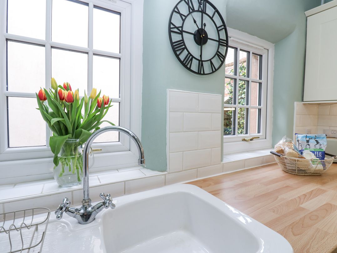 A kitchen sink with a vase of tulips on the windowsill and a countertop with a basket of groceries at 3 Eden View in Lazonby