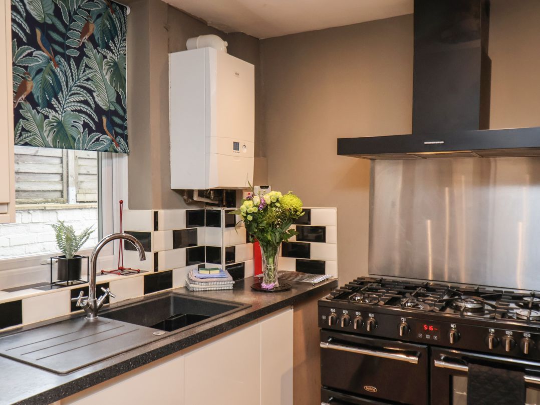 A kitchen with a black gas stove and oven a black sink with a silver faucet a bouquet of flowers on the counter and a window with a patterned blind at Sail Lodge in Scarborough