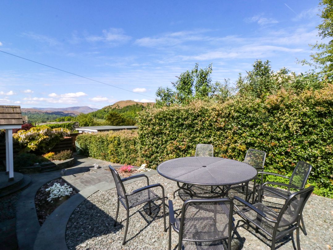An outdoor patio with a round metal table and six metal chairs surrounded by gravel and greenery at Beckside in Ambleside