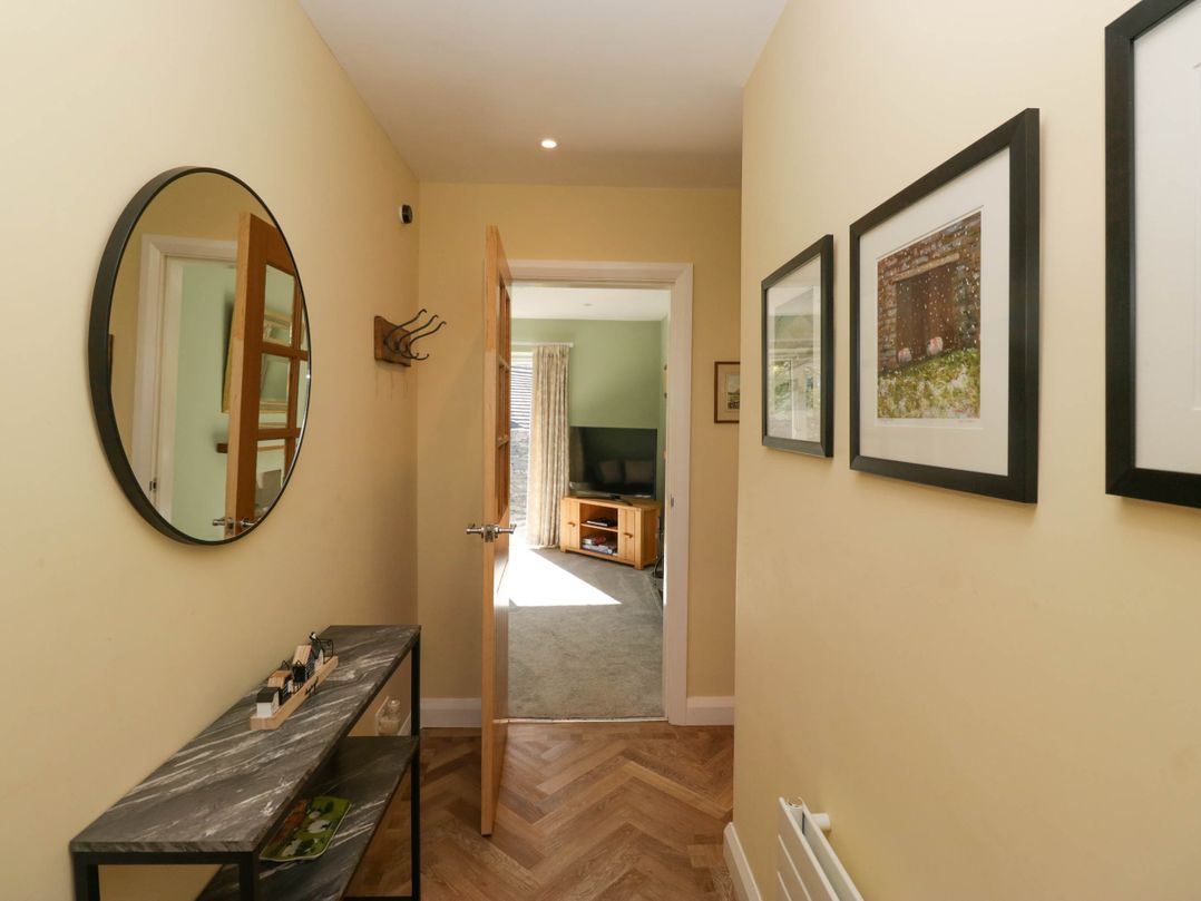 A hallway with a round mirror and console table leading to a room with a TV at Beckside in Ambleside