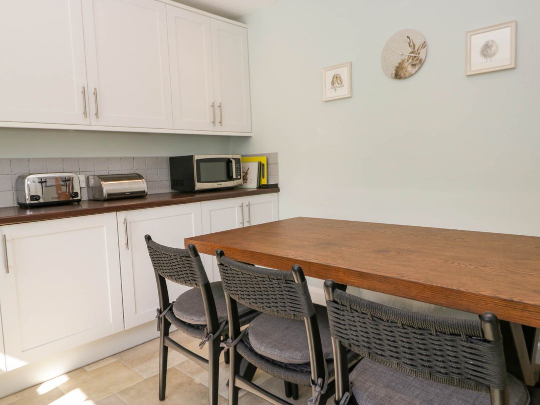 A kitchen with white cabinets a wooden table three black chairs a microwave toaster and bread box on the counter at Beckside Ambleside