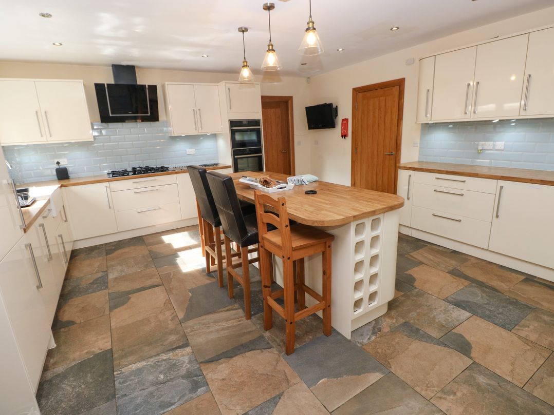 A kitchen with an island and bar stools at Ty-Gan Dderwen in Llangennech, Llanelli