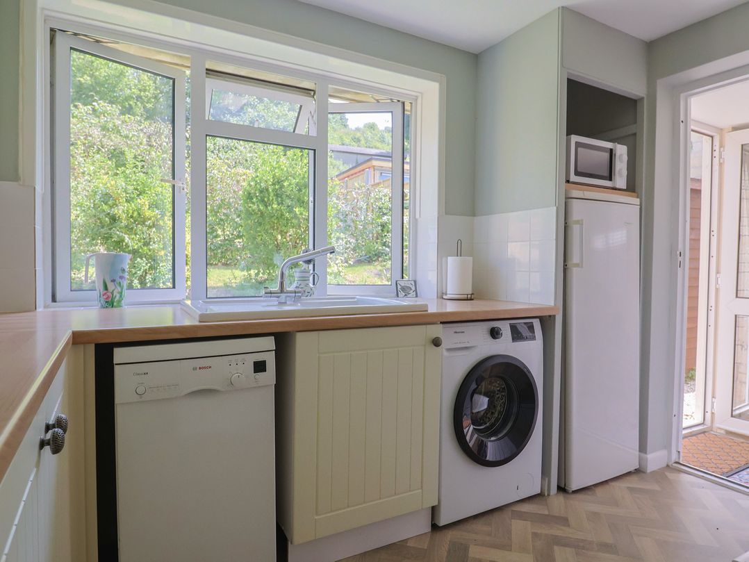 A kitchen with a window, sink, dishwasher, washing machine, and fridge at Tane in Winterborne Stickland