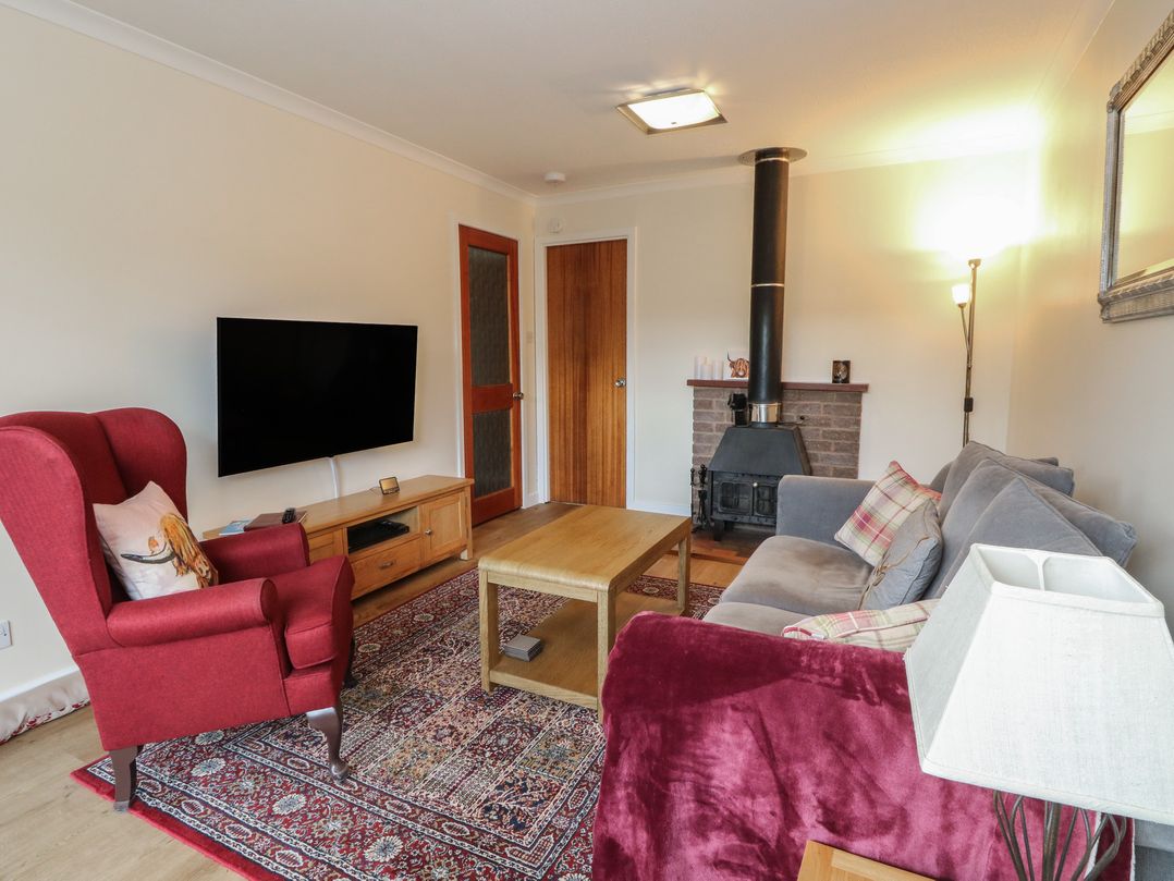 A living room with a sofa, armchair, and television at Steam Cottage in Aviemore