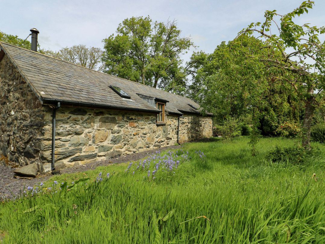 A stone cottage surrounded by grass and trees at Bythyn Ddol Hafod, Capel Curig
