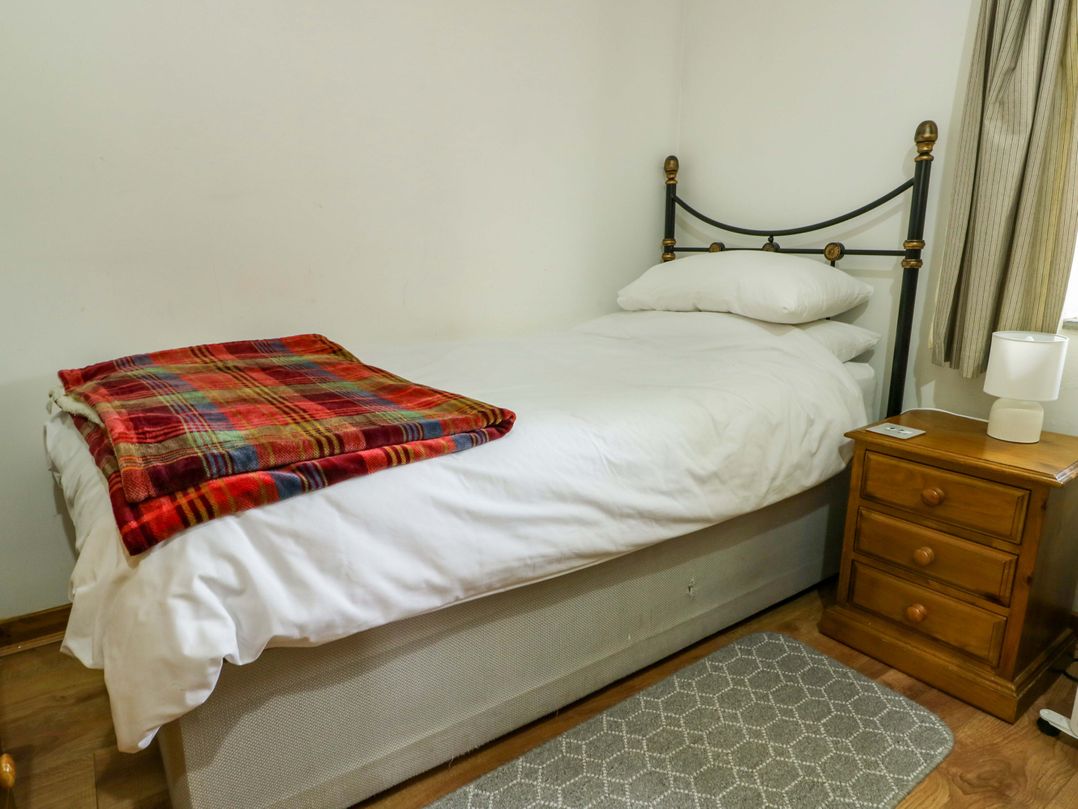A bed with a blanket and nightstand at Bythyn Ddol Hafod in Capel Curig