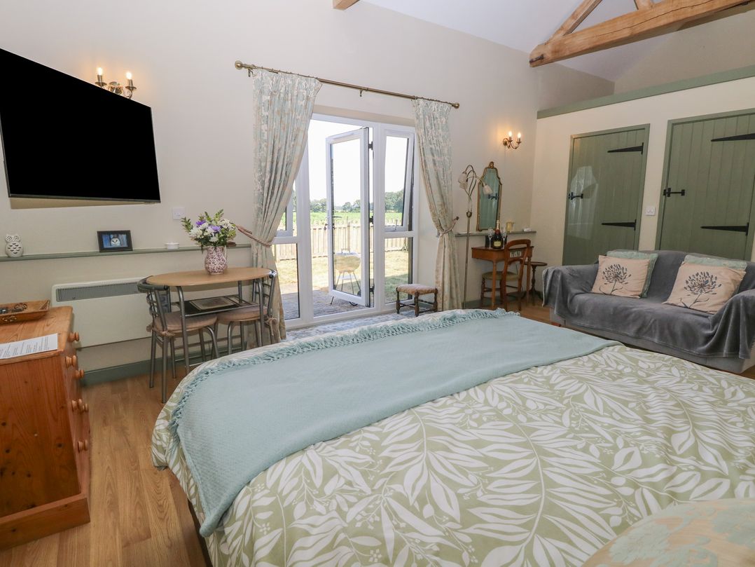 A bedroom with a bed, sofa, table, and doors leading outside at Tawny Owl Barn Shipdham near Dereham