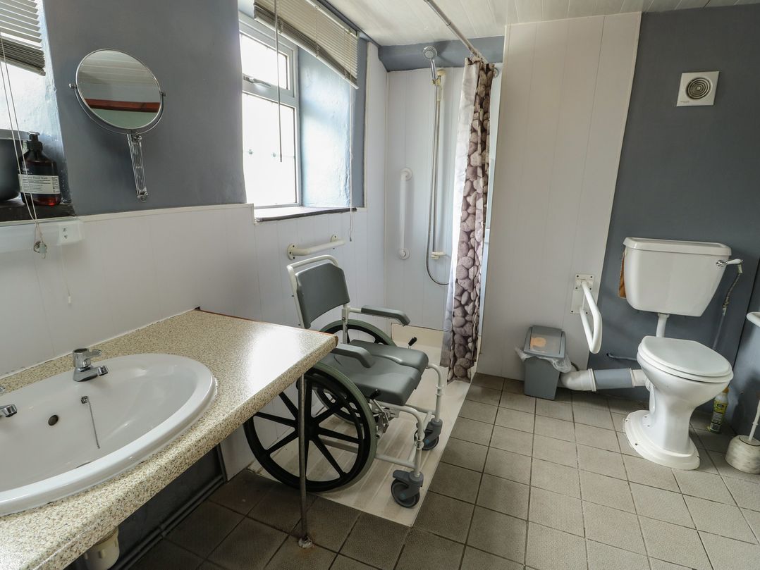 A bathroom with a sink, toilet, shower, and wheelchair at Glan y Gors in Dinorwic near Llanberis