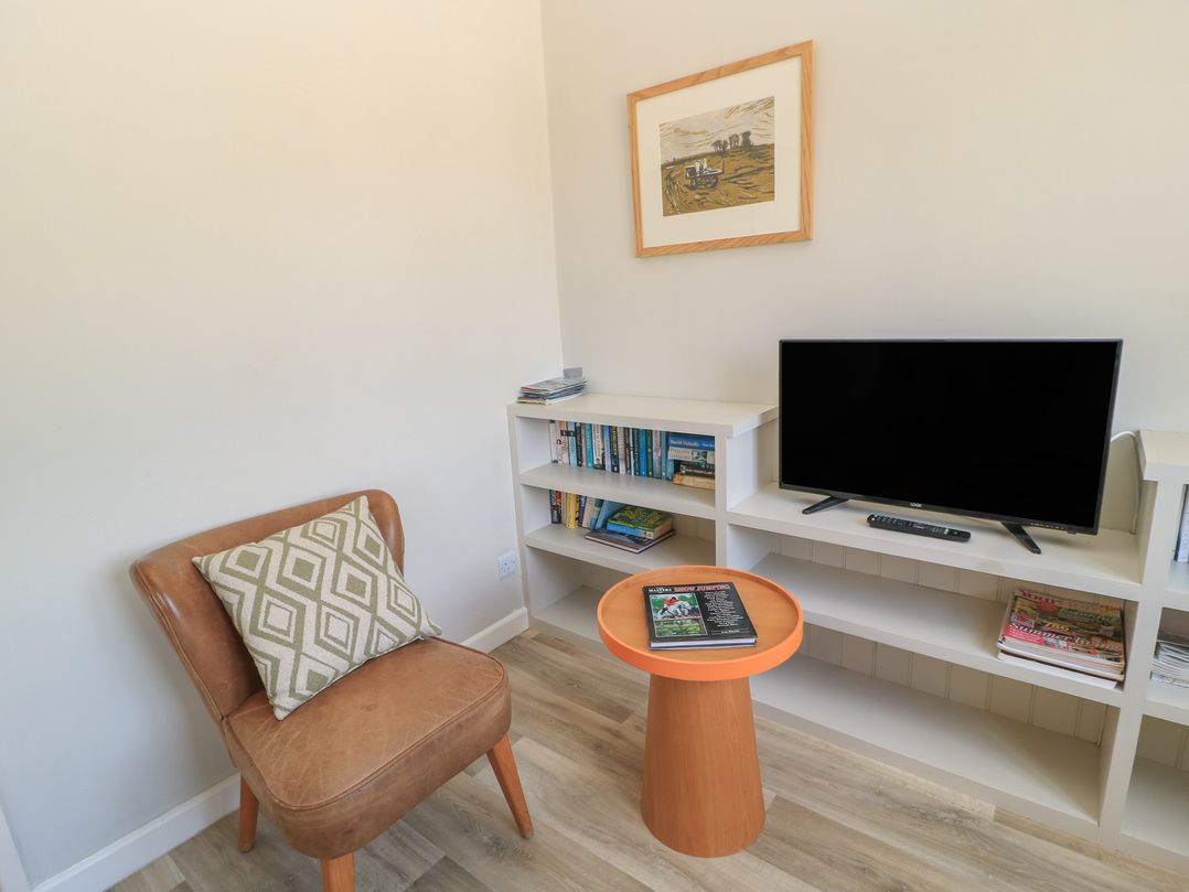 A living room with a chair, television, and bookshelf at The Apple Shed, Motcombe