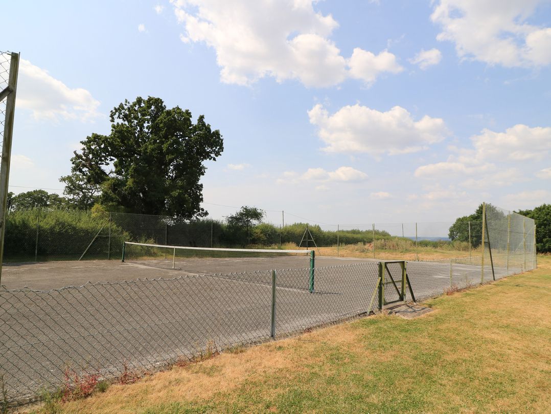 A tennis court with a net and fence at The Apple Shed, Motcombe
