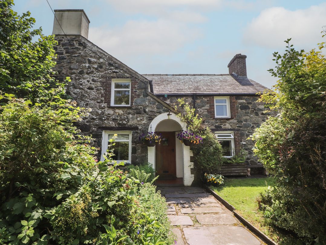 A stone house with a garden and pathway at Plas Mawr in Groeslon