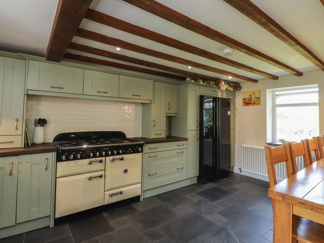 A kitchen with cabinets, stove, refrigerator, and dining table at Plas Mawr in Groeslon
