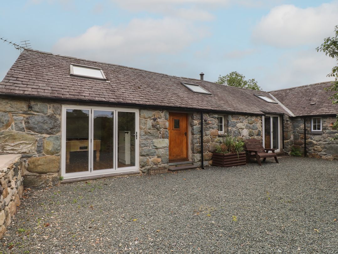 An outdoor area with a stone building and sliding glass doors at Beudy'r Wennol Groeslon