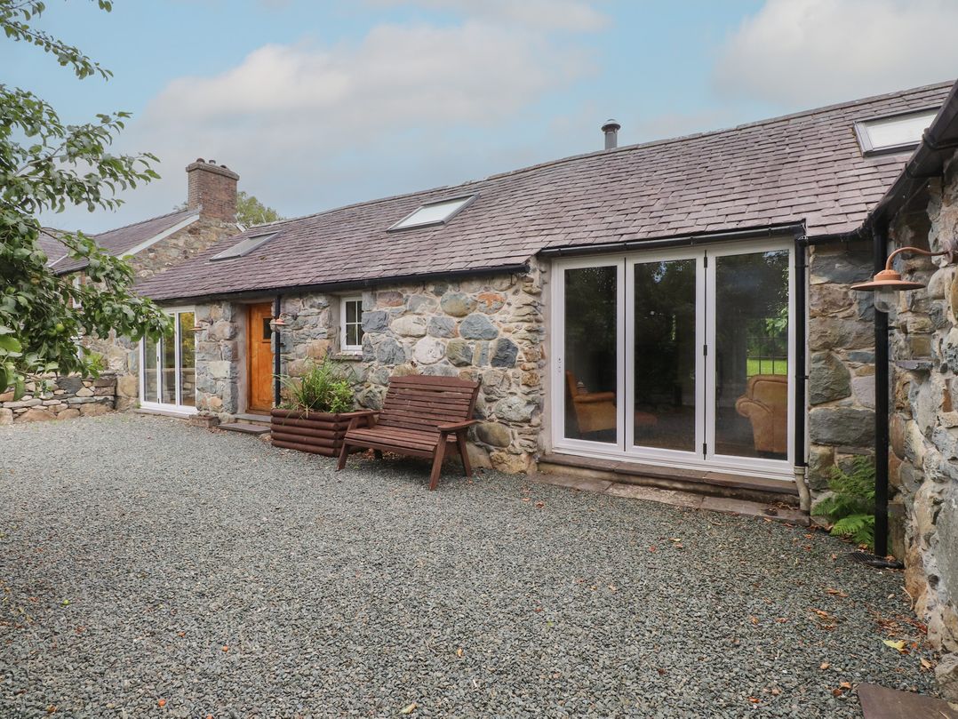 An outdoor area with a wooden bench and stone walls at Beudy'r Wennol, Groeslon