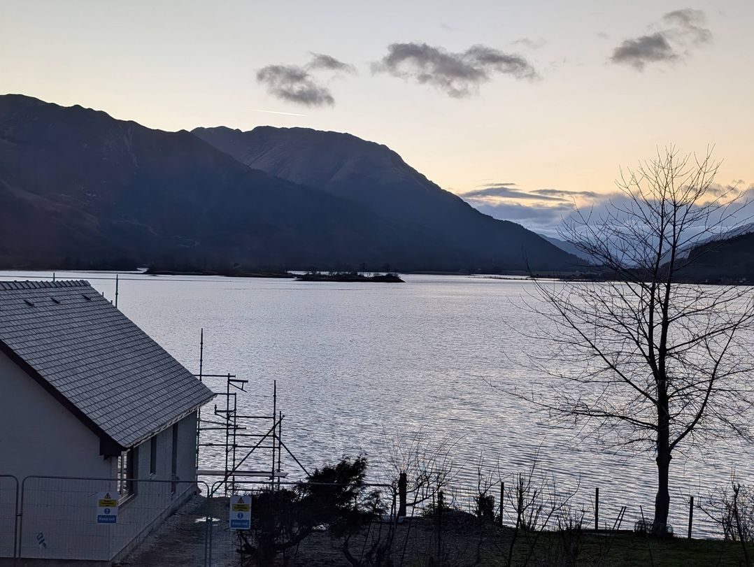 A view of a lake and mountains with a house and tree at Callart View in Glencoe