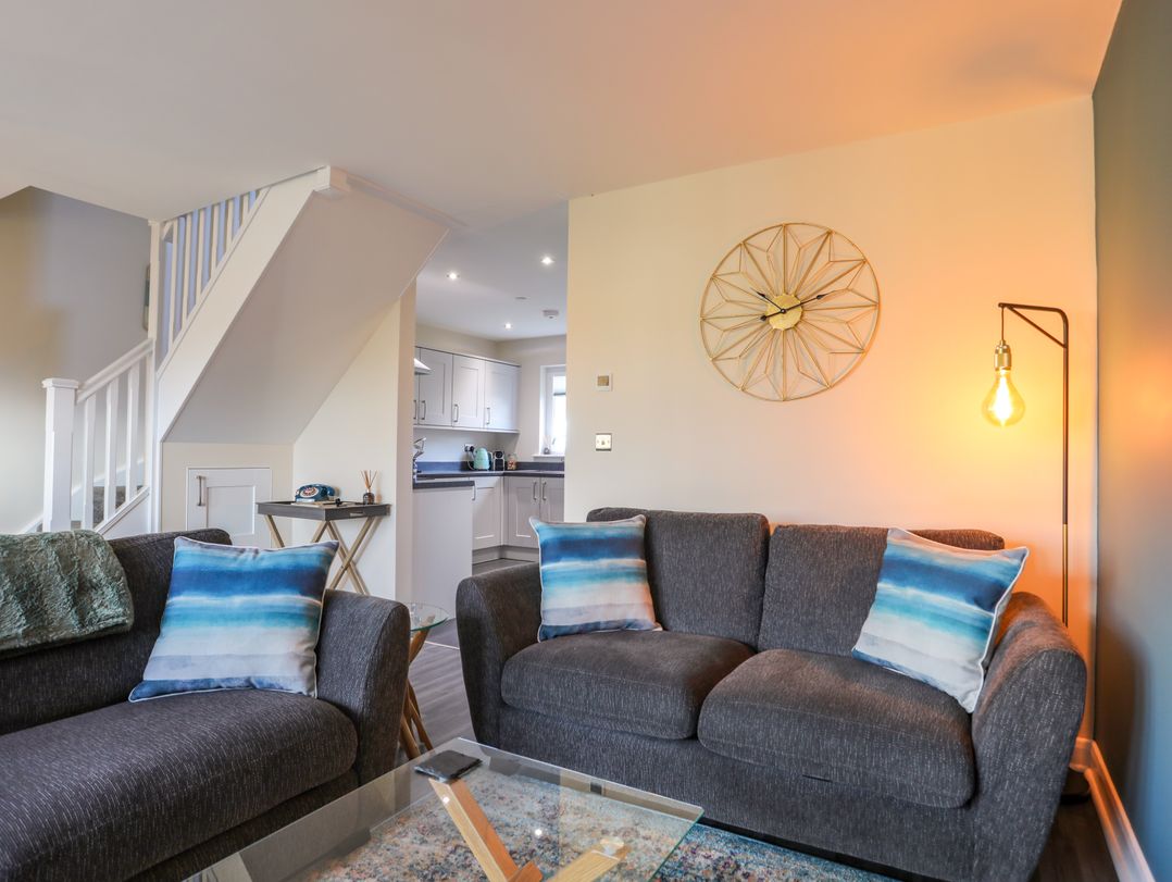 A living room with two gray sofas with blue and white cushions a glass coffee table and a floor lamp at 19 Parc Delfryn in Benllech