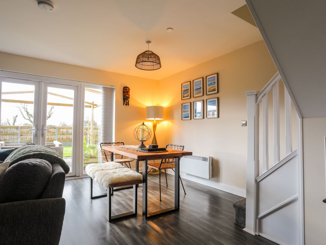 A dining area with a wooden table and chairs near glass doors leading to a garden at 19 Parc Delfryn in Benllech