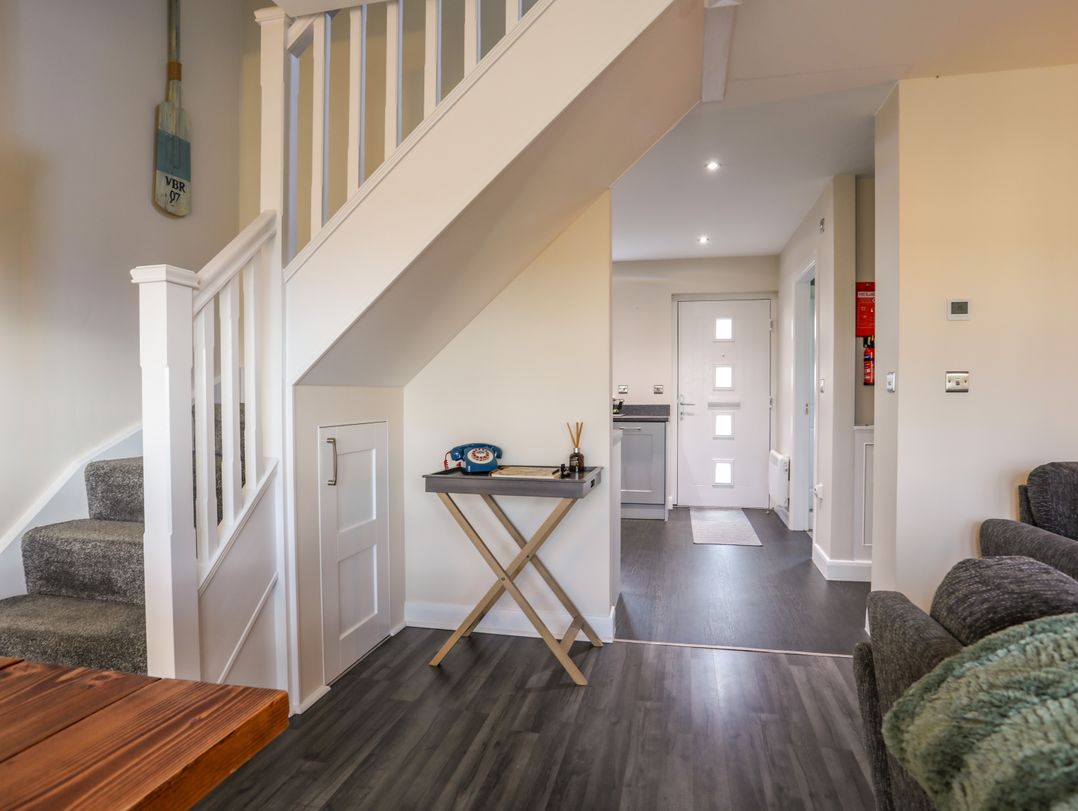 A hallway with stairs, a small table with a vintage phone, and a door leading to another room at 19 Parc Delfryn in Benllech