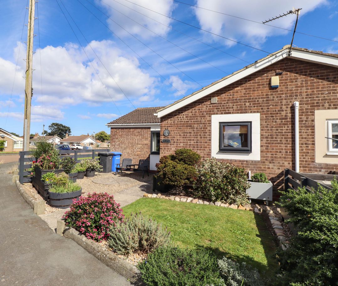 An outdoor area with flower beds and a house at Flora Cottage Beadnell