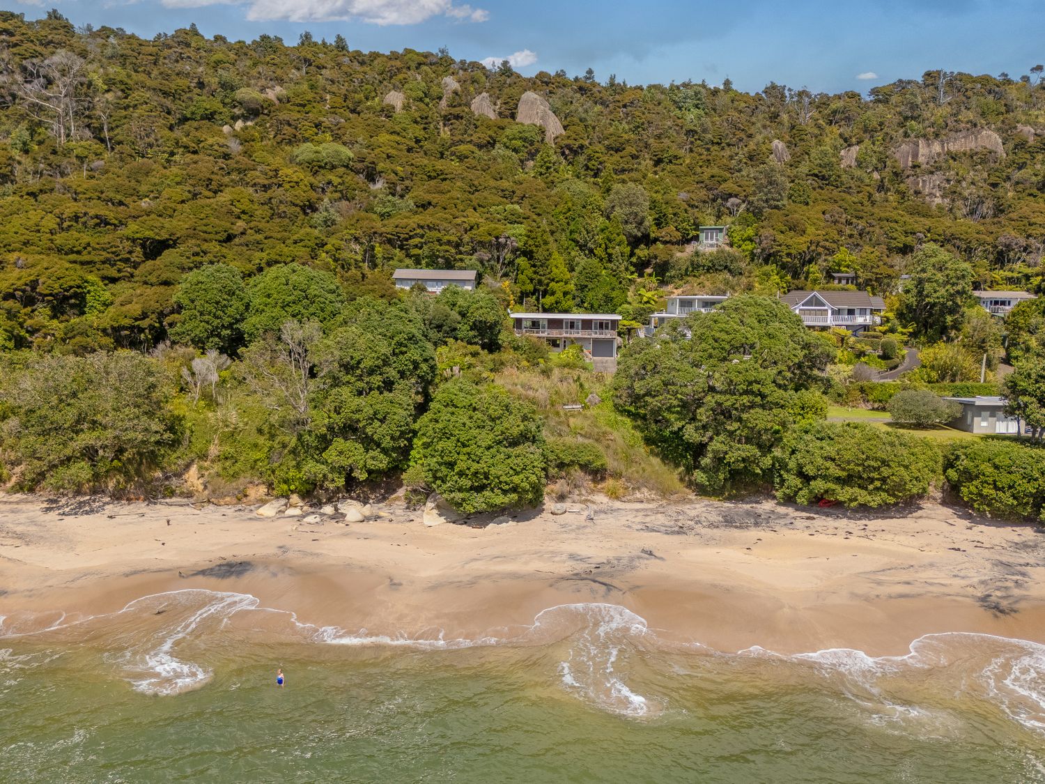 A beach with waves coming onto the sand and houses behind trees on a hillside at The Retreat - Front Beach Bach in Front Beach