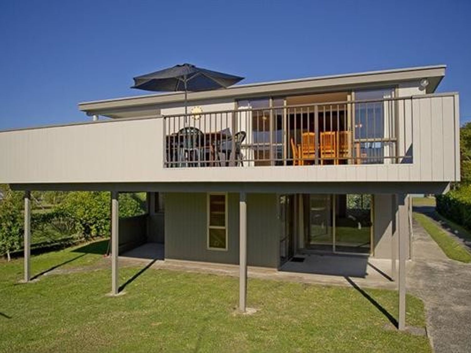 A two-story house with a balcony featuring outdoor furniture and an umbrella at Joes Place - Cooks Beach Holiday Home in Cooks Beach