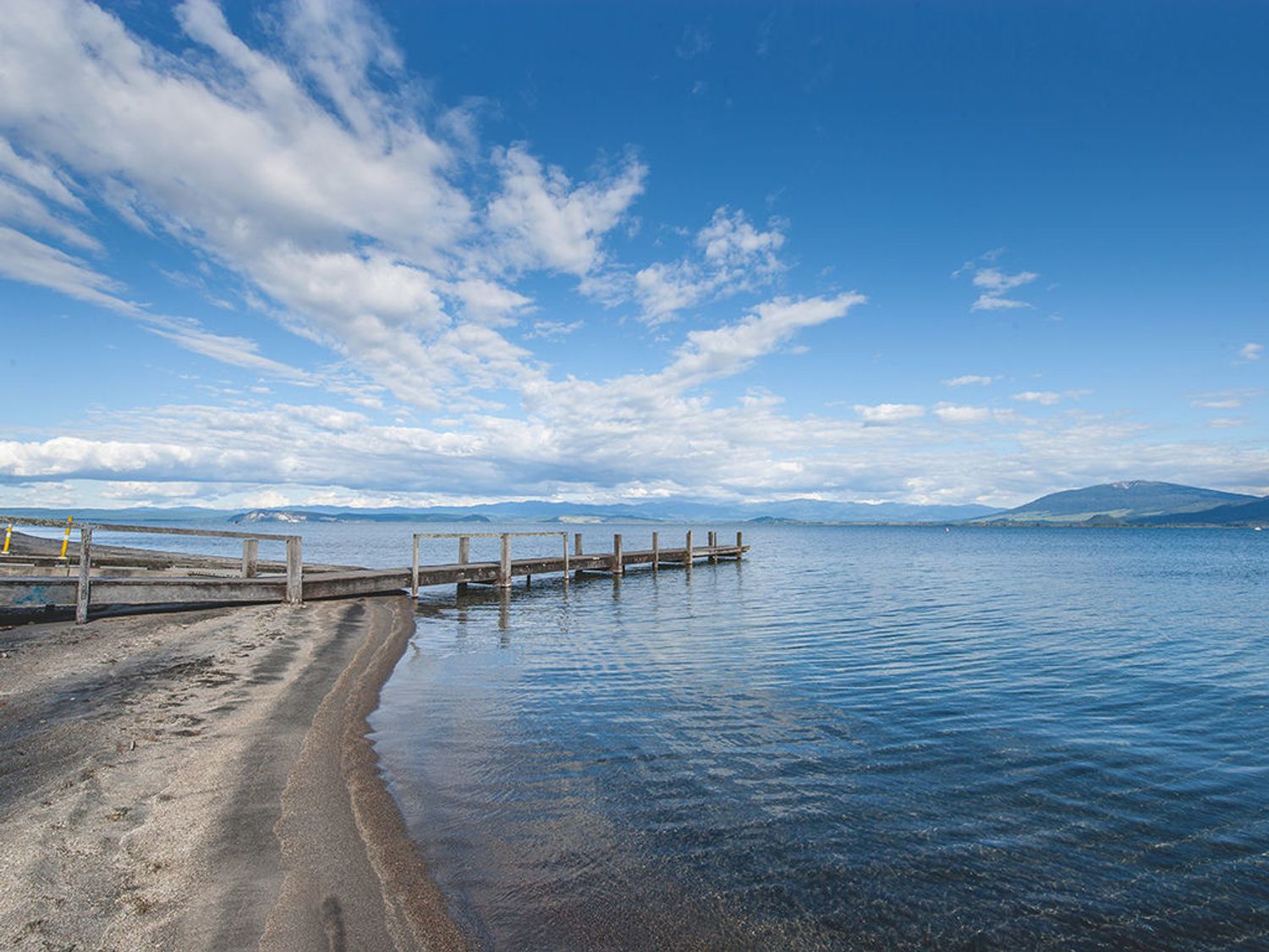 A wooden pier extending into a lake with mountains and clouds in the background at Little Lockwood - Kuratau Bach in Kuratau