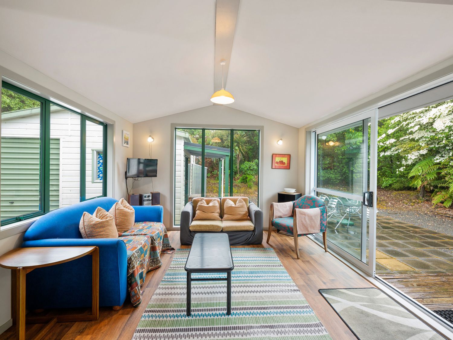 A living room with blue and beige sofas a patterned rug and sliding glass doors at Little Lockwood - Kuratau Bach in Kuratau