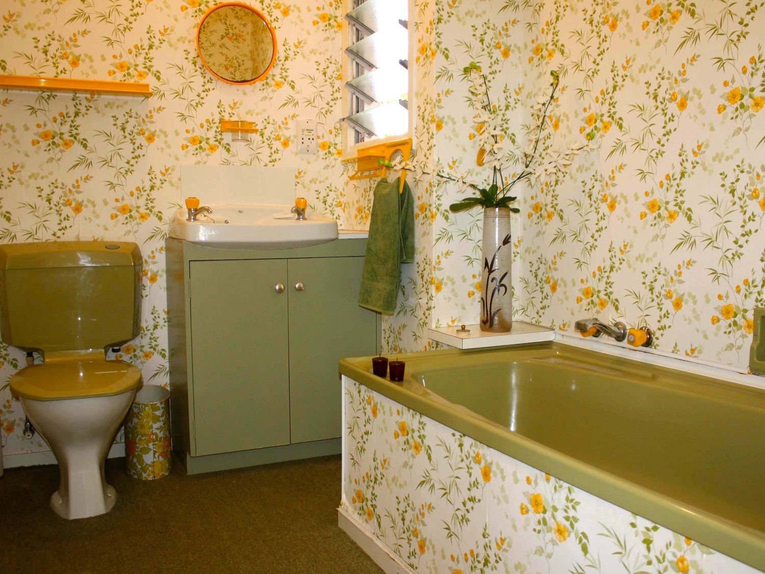 A bathroom with a green toilet green bathtub a sink vanity and floral wallpaper at Moeroa - Wharewaka Holiday Home in Wharewaka